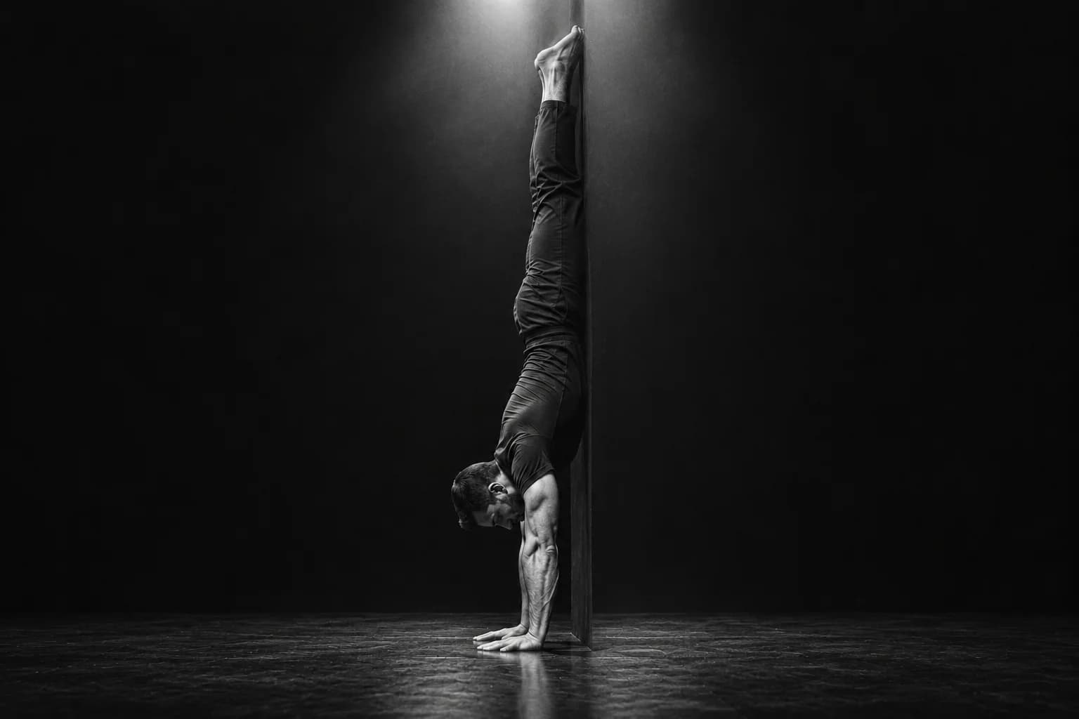 A man doing a chest-to-wall handstand on a dark stage