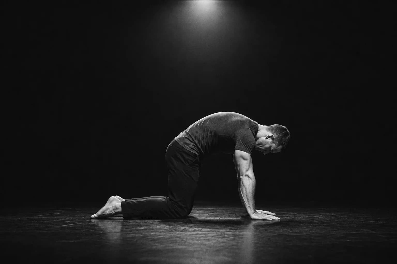 A man on all fours doing the cat-cow exercise on a dark stage